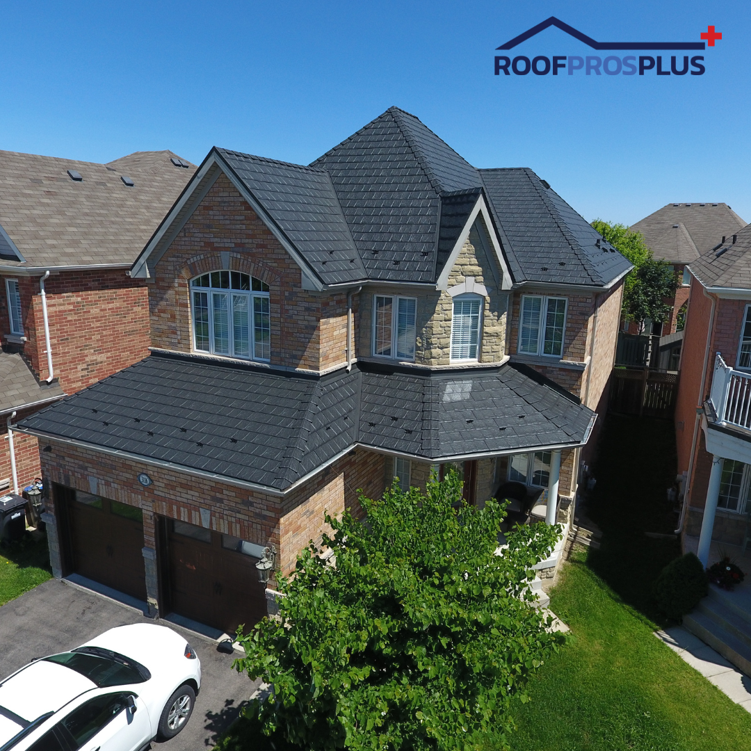 A brick house with a new, dark metal roof under a clear blue sky. A white car is parked in the driveway.