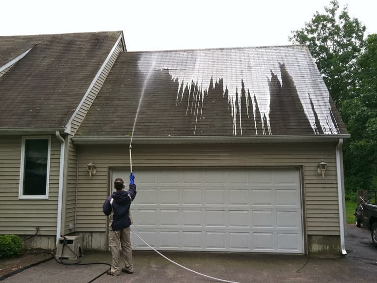 A picture of a professional, spray cleaning a residential roof.