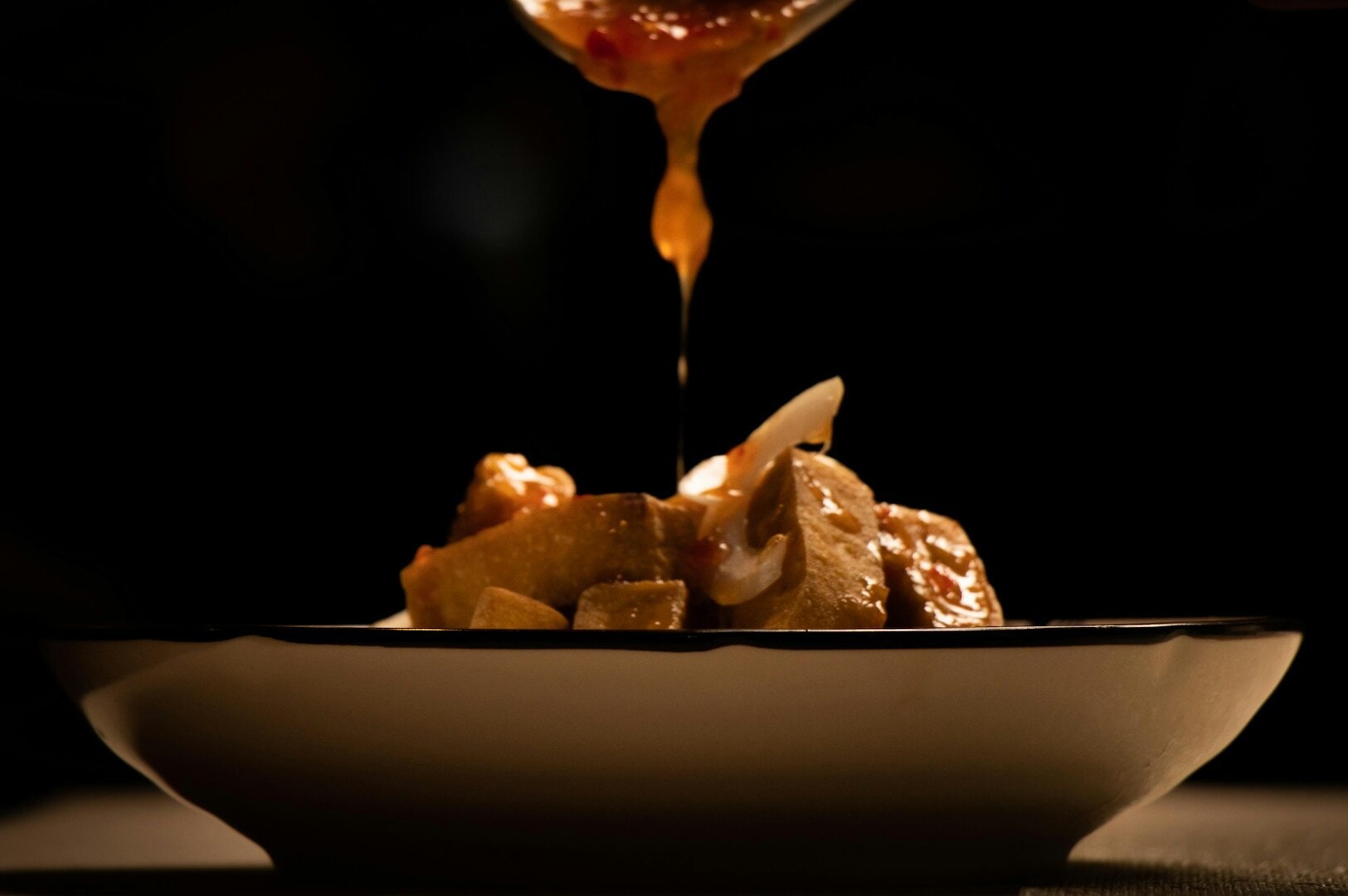 A spoon is being poured over a bowl of food, showcasing a delicious dish served in a Singapore restaurant.