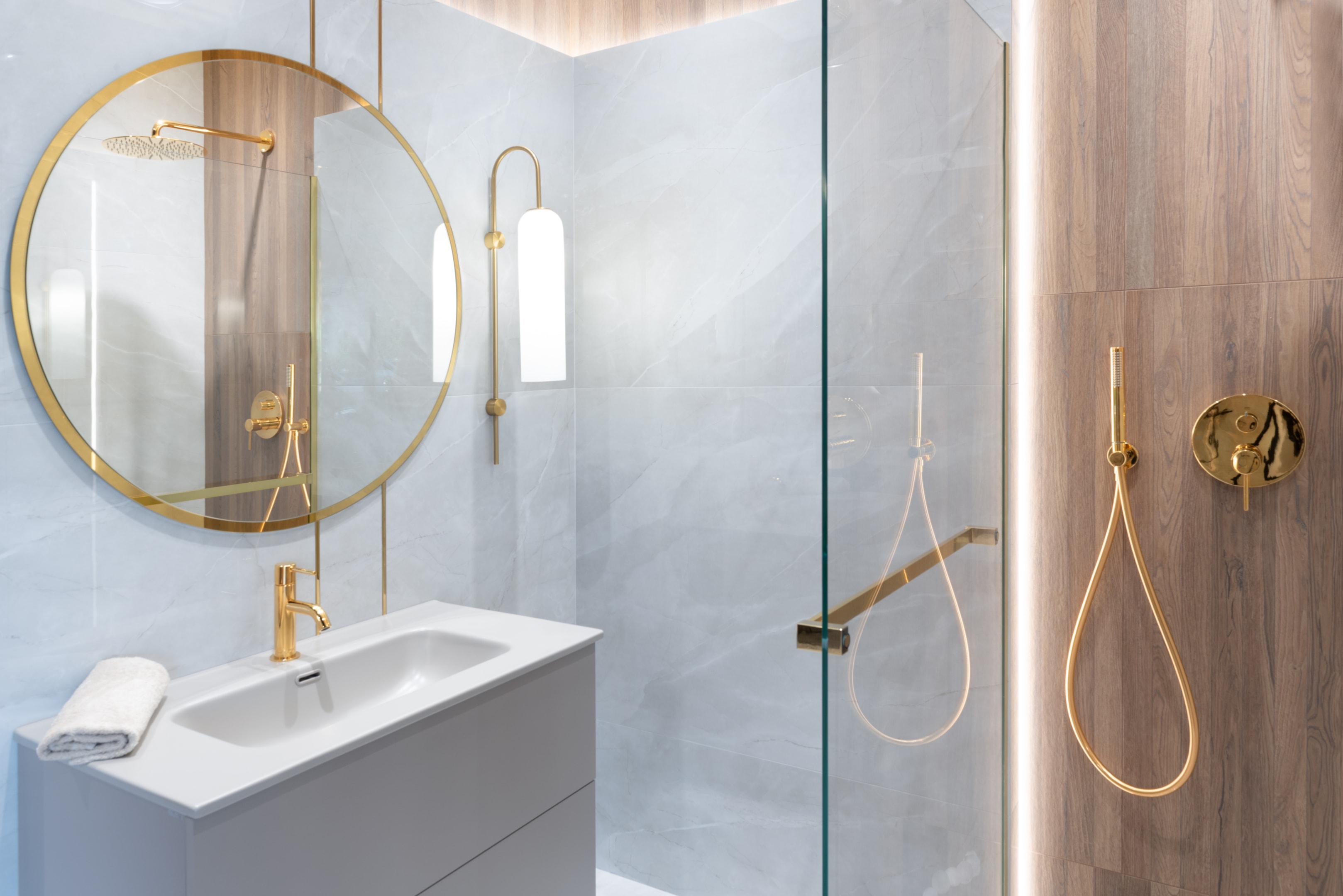 Elegancka łazienka glamour z szarymi płytkami, złotą armaturą i okrągłym lustrem