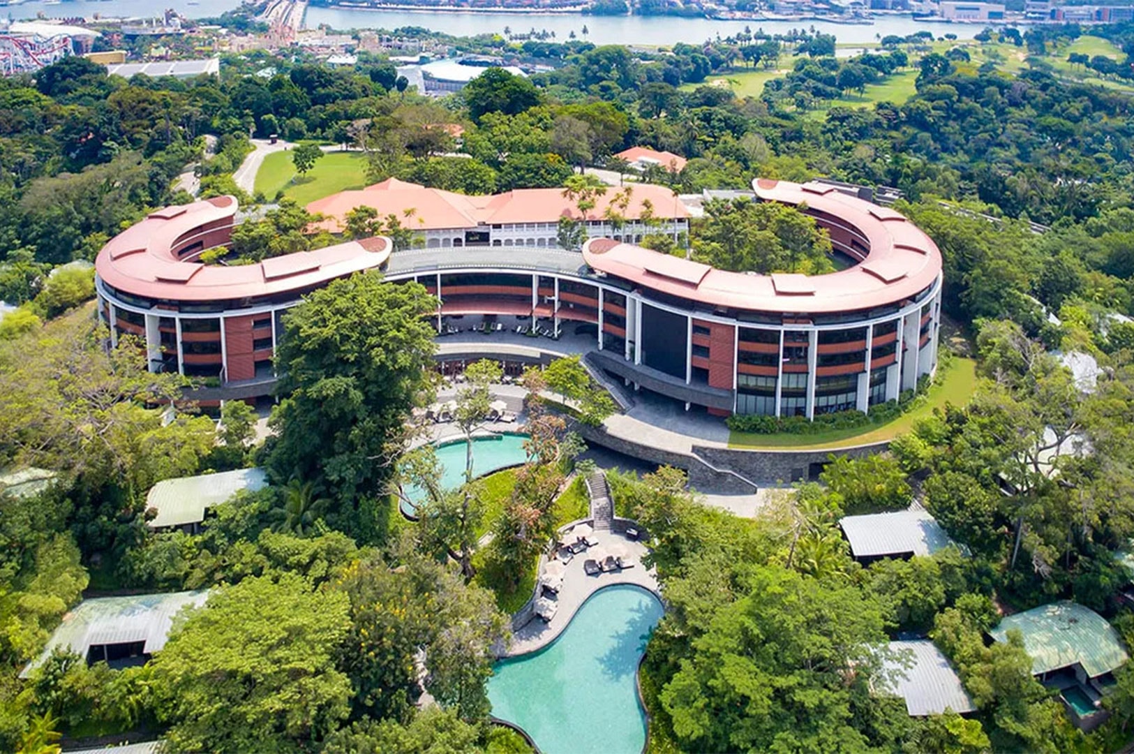 Aerial view of Capella Singapore, featuring curved buildings surrounded by lush greenery and outdoor pools.