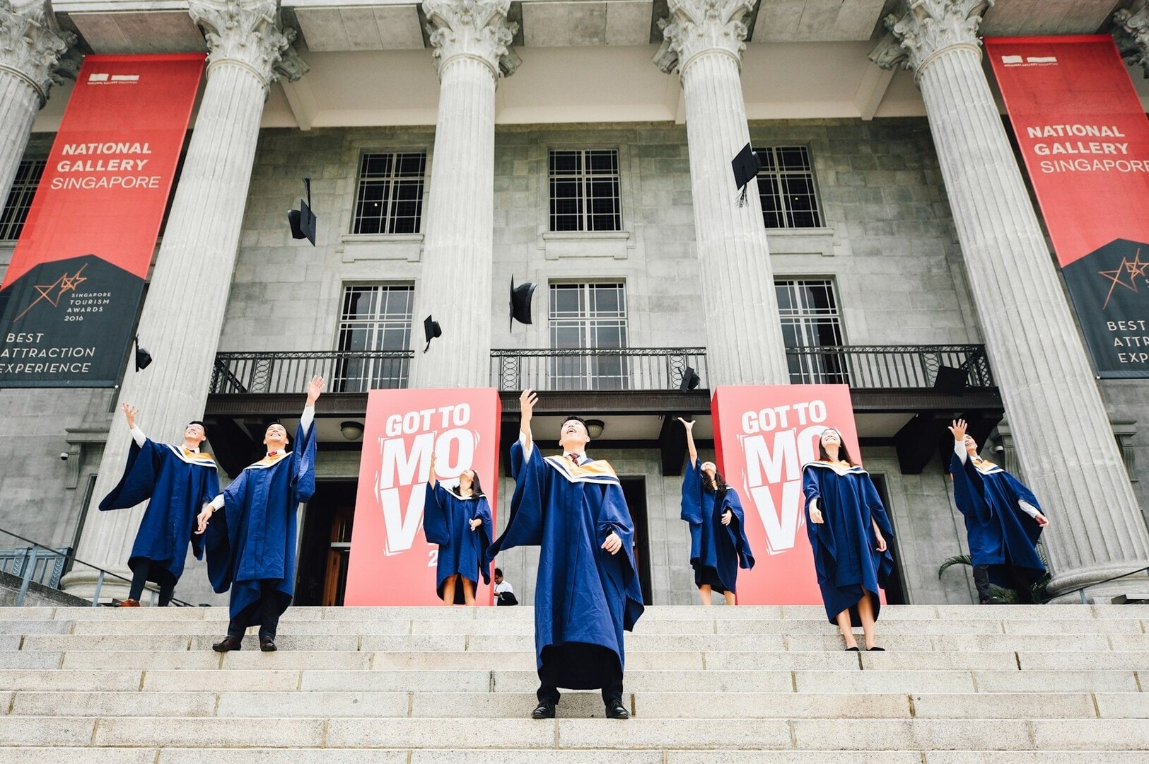 Graduates in gowns pose on the steps of a building at Singapore University Campus, celebrating their achievements.