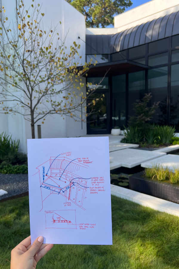 a woman's hand holds up a drawing of a building facade in front of that facade