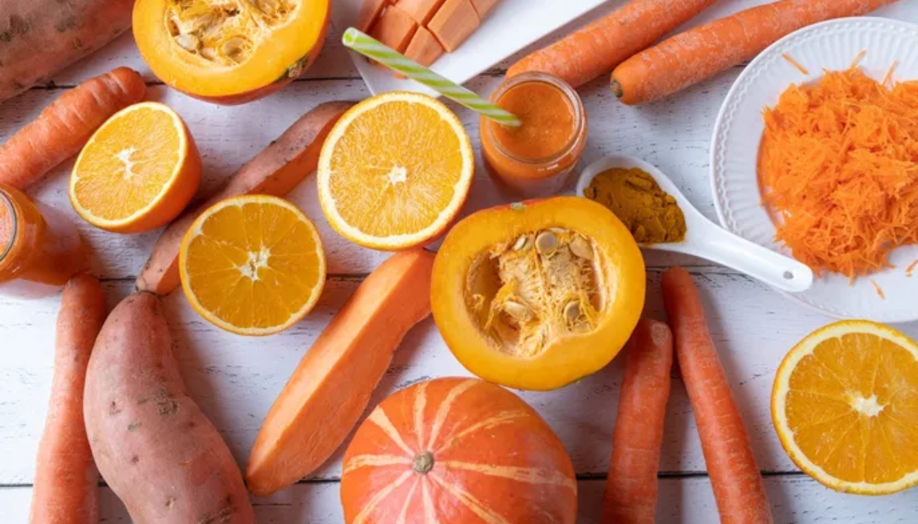 Blandede oransje matvarer som gulrøtter, gresskar, appelsiner og søtpotet på hvitt bord, rike på betakaroten og vitaminer.