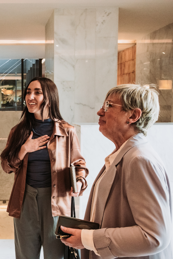 an older woman and a young woman look toward a person not pictured in a lobby