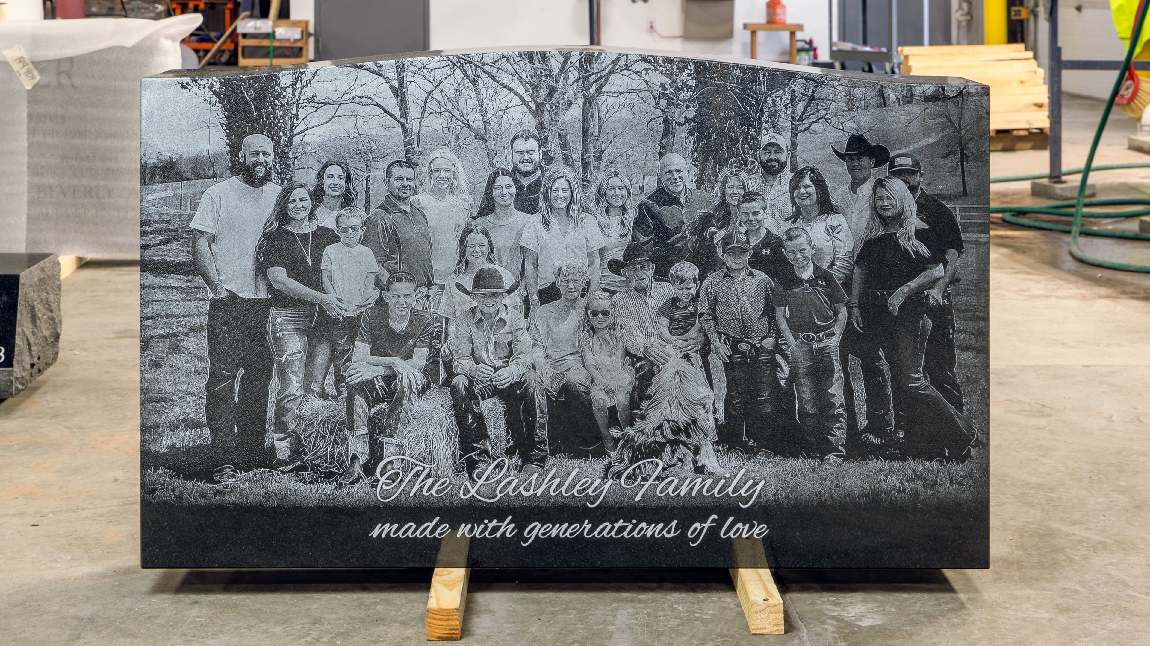 A large black granite headstone featuring a detailed laser-etched family portrait with multiple generations posing outdoors. The engraving reads “The Lashley Family – made with generations of love,” demonstrating the clarity and high resolution of modern laser etching on stone.