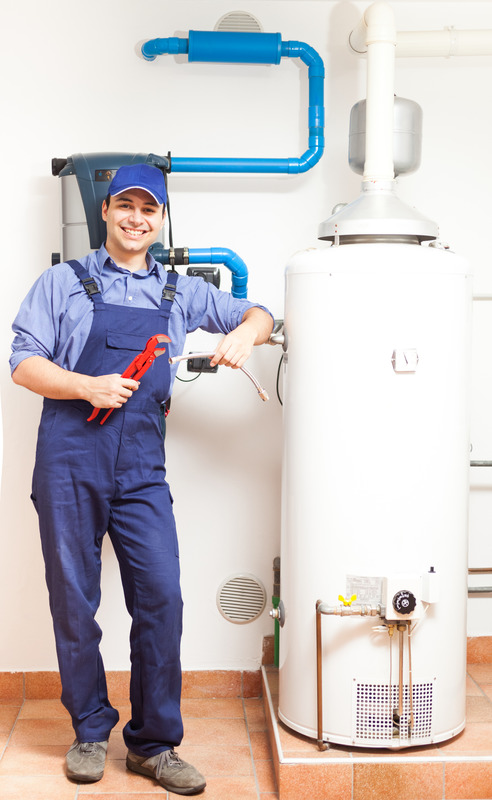 Lächelnder Installateur in Arbeitsuniform mit Werkzeug neben einer Gastherme