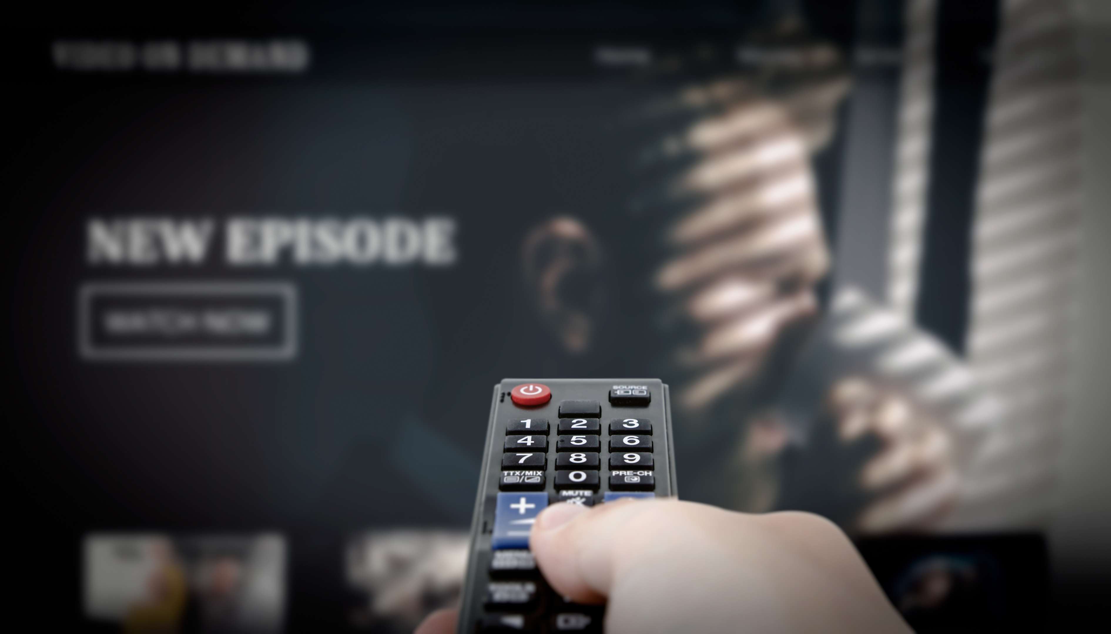 a hand points a tv remote at the tv screen that shows a new episode of a TV series