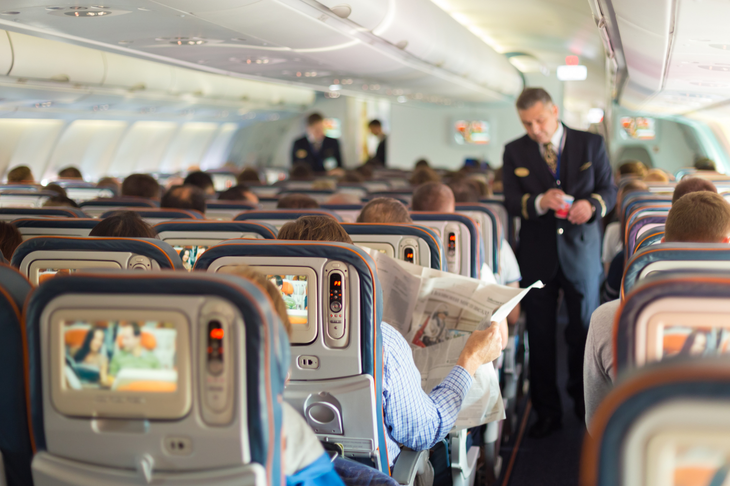 a male pilot walking in the isle inside the flight and passengers being seated 