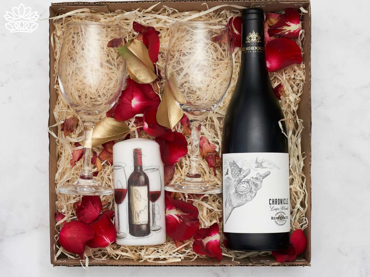 A wine gift box containing a bottle of wine, two glasses, and a candle, with rose petals and golden leaves. Flowers with Champagne & Wine. Delivered with Heart. Fabulous Flowers and Gifts.