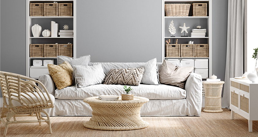 This living room shows a modern take on the classic Hamptons style, the linen-covered off-white couch perfect for lounging is decorated with a variety of neutral throw pillows. Wicker baskets and sea-inspired decorations are displayed in built-in shelves. Wicker and cane furniture is displayed to keep with the coastal style of the Hamptons.