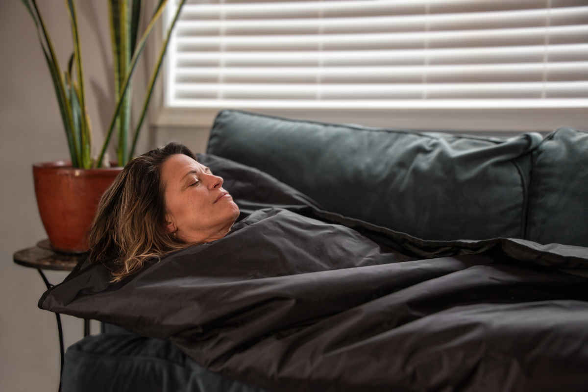Lady laying on a couch inside of a far infrared sauna blanket in black