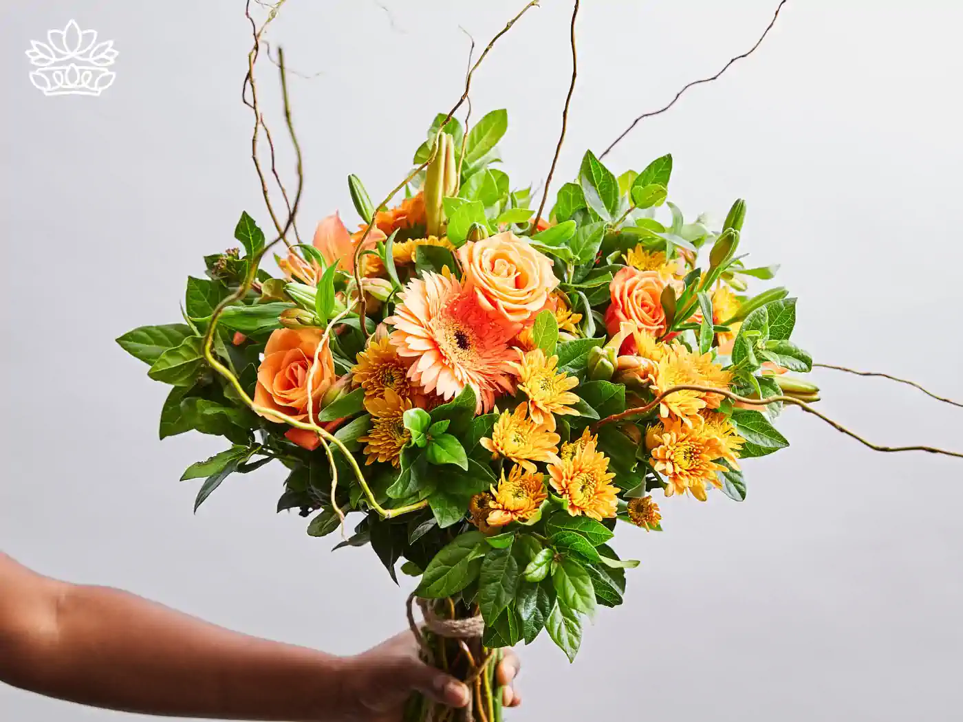 Hand holding a cheerful get well bouquet of orange roses and yellow daisies, interlaced with vibrant green leaves and delicate twigs, conveying warmth and well-wishes. Delivered with Heart. Fabulous Flowers and Gifts.
