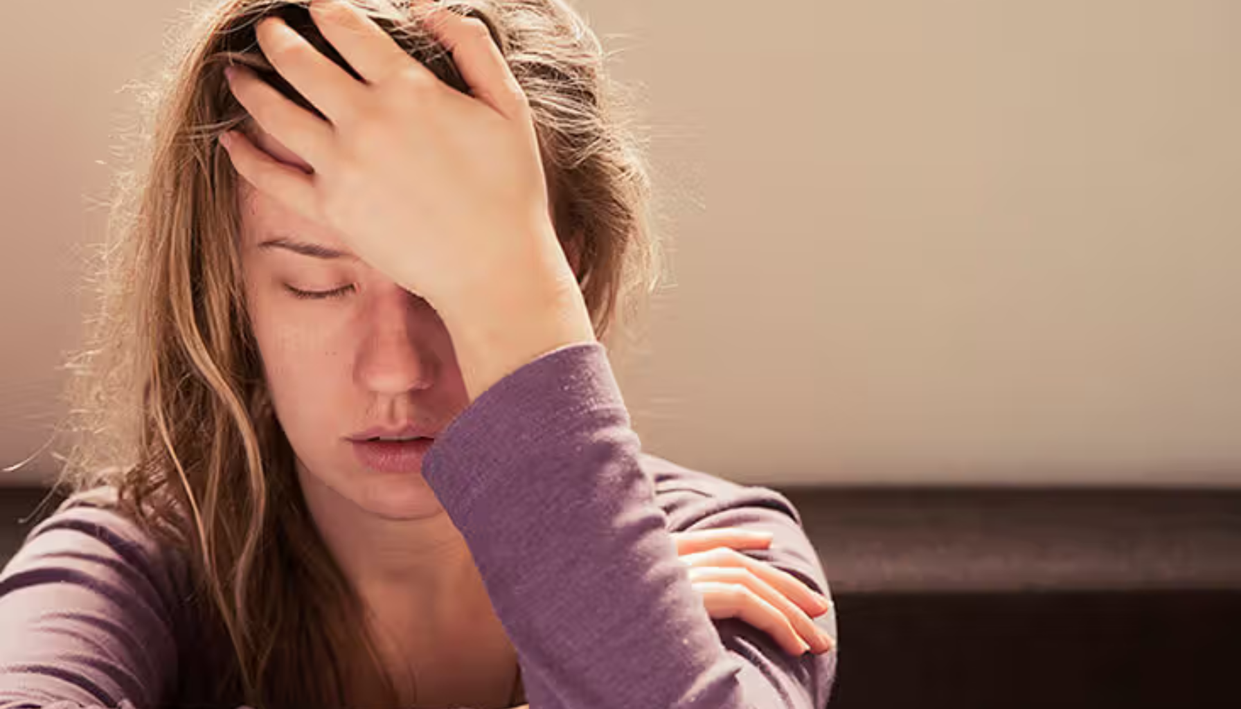 Kvinne med lukket øyne holder hånden mot pannen, tydelig utslitt og plaget av intens hodepine eller stress.