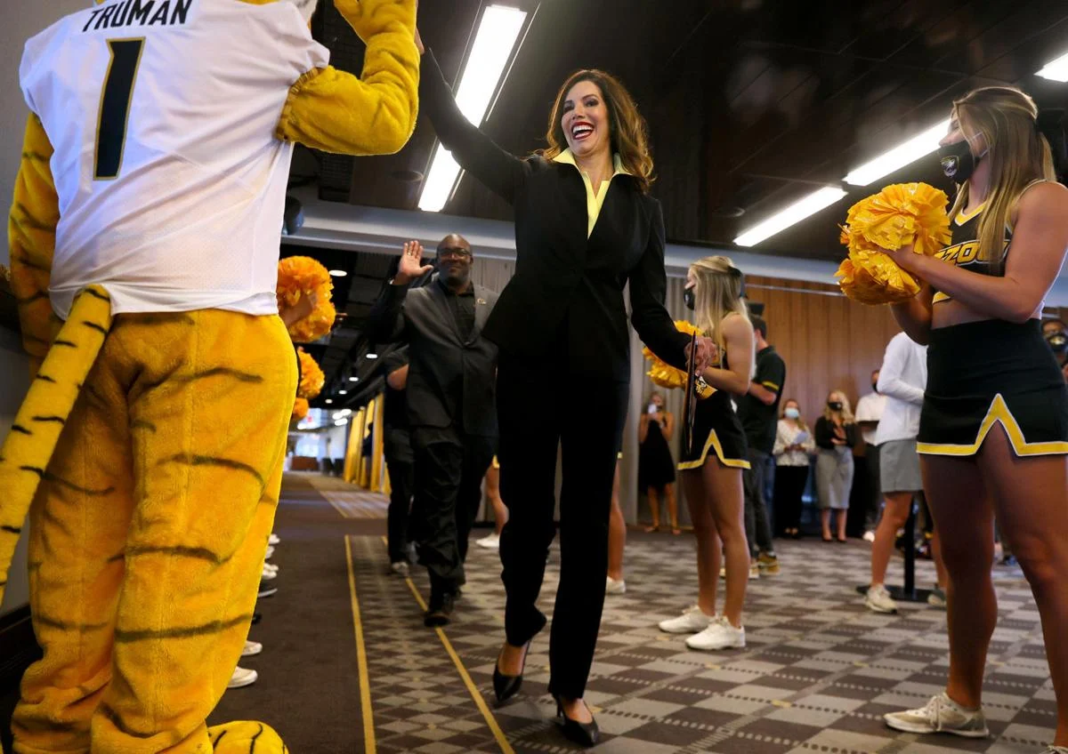 University of Missouri administrator high-fiving Truman the Tiger mascot while walking past cheerleaders, celebrating a university NIL-related event.