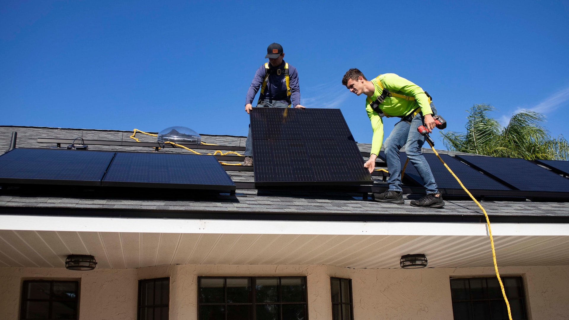 Professional electricians installing solar panels on a roof, as part of a solar EV charging station. 