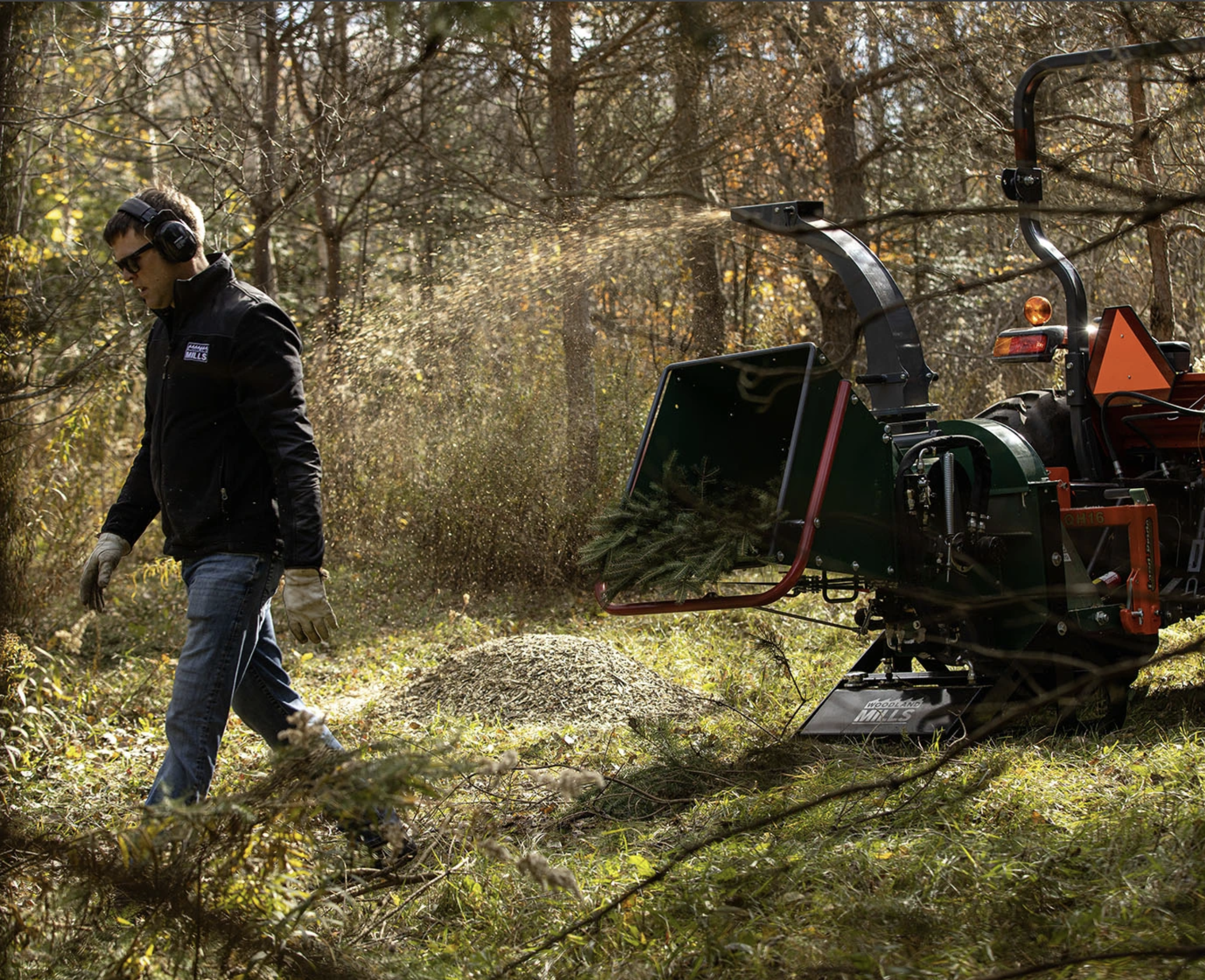 A man walking away from a Woodland Mill WC88 Wood Chipper as it chips a tree branch in a forest.