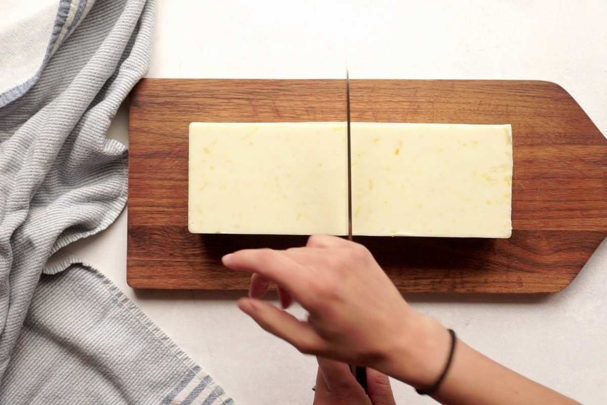 loaf of soap on wooden cutting board being sliced into bars
