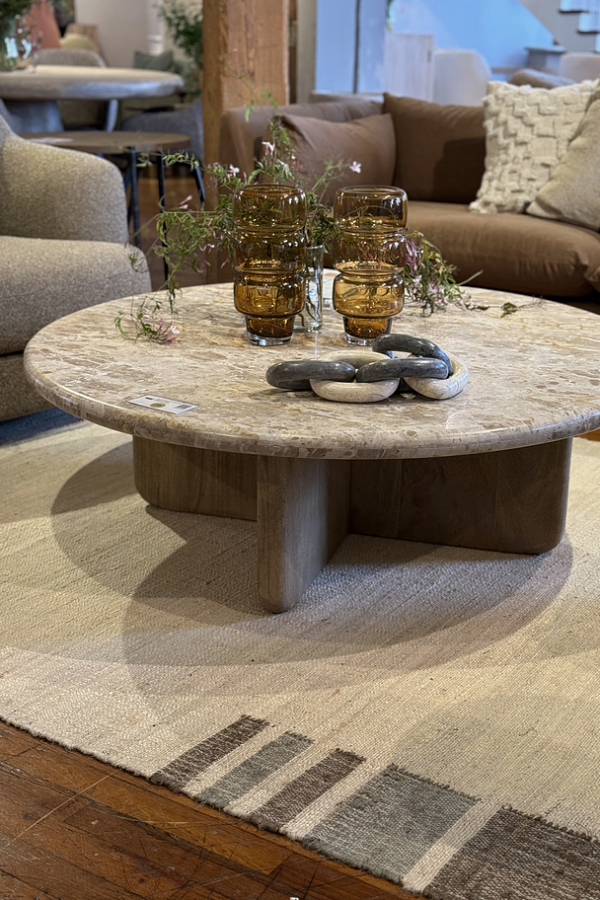 Round stone coffee table styled with amber glass vases and a sculptural chain object on a neutral rug.