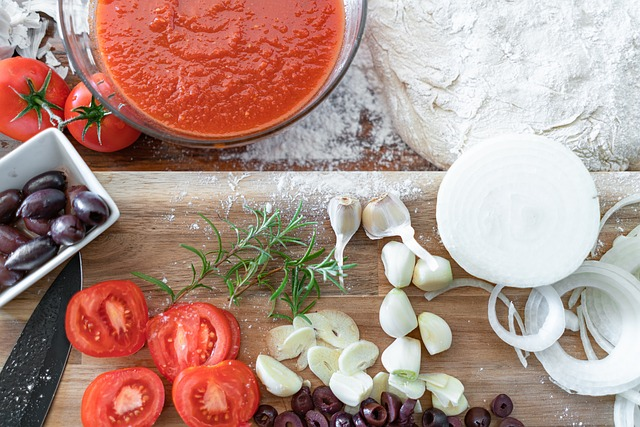 pizza ingredients such as tomatoes, tomato sauce, olives, garlic, rosemary and onions with pizza dough on the side