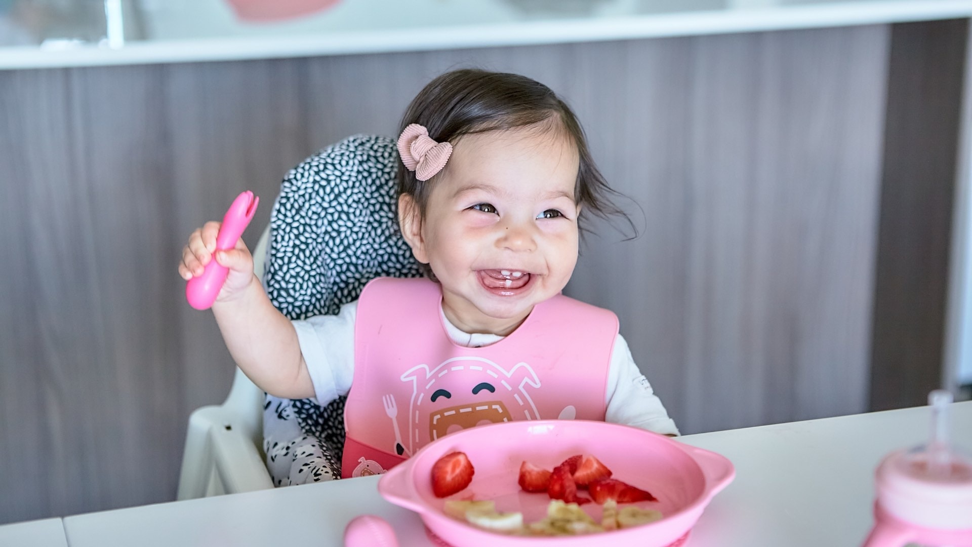 A baby, wearing just a diaper, is reaching excitedly for a variety of colorful vegetables on a family dinner table, showcasing the concept of baby led weaning. The scene highlights the introduction of solid foods, encouraging self-feeding and the exploration of different foods during family mealtime.