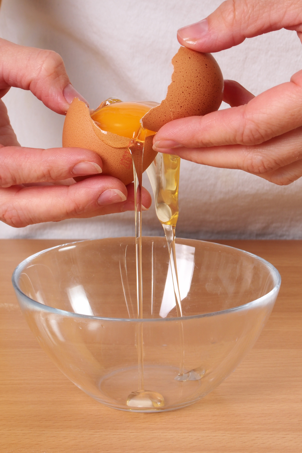 hands tossing yolk back and forth with egg shell over a small bowl