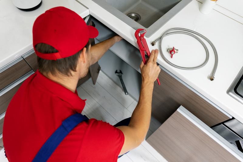 Installateur in roter Arbeitskleidung repariert Wassergebrechen in der Küche