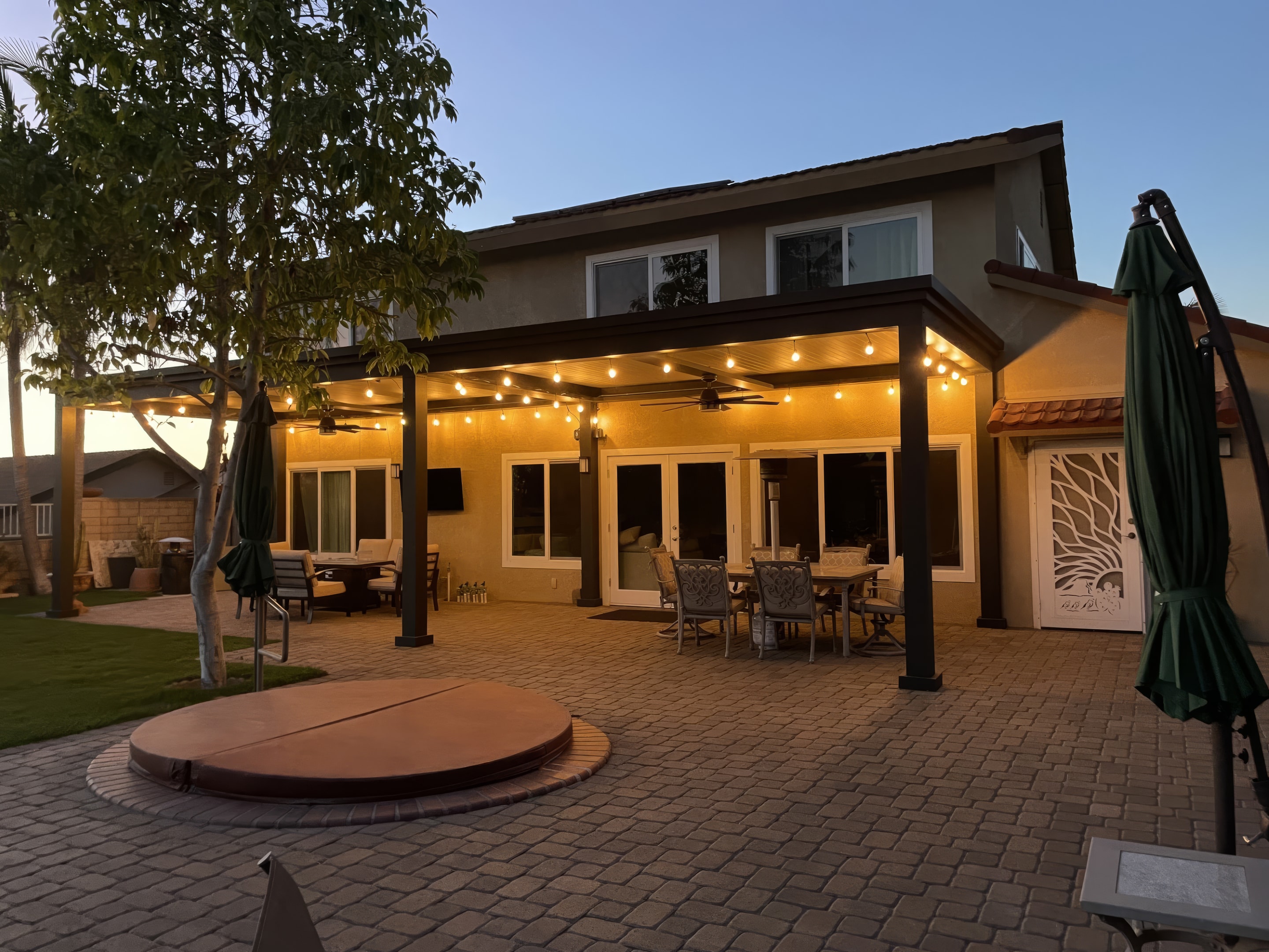 Finished outdoor living space remodel, with upgraded hardscape, hot tub, pergola, outdoor lighting, and outdoor seating.