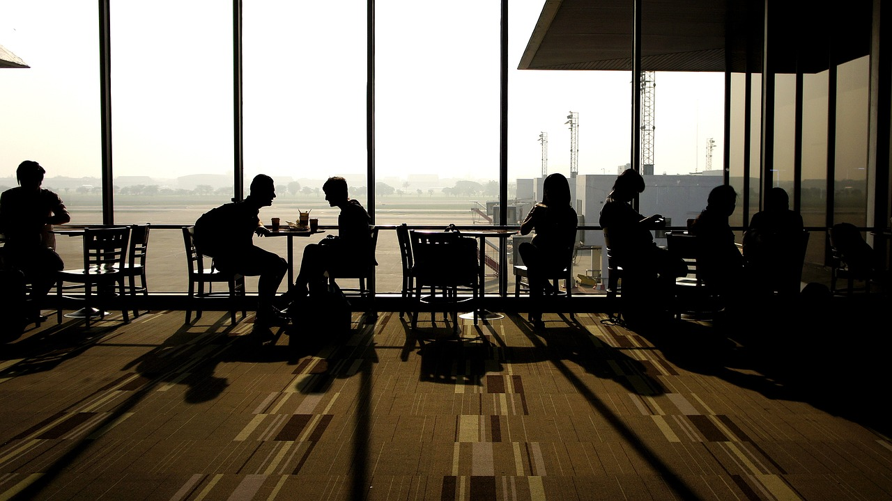 A number of passengers sitting an at airport cafe eating and watching aircraft.