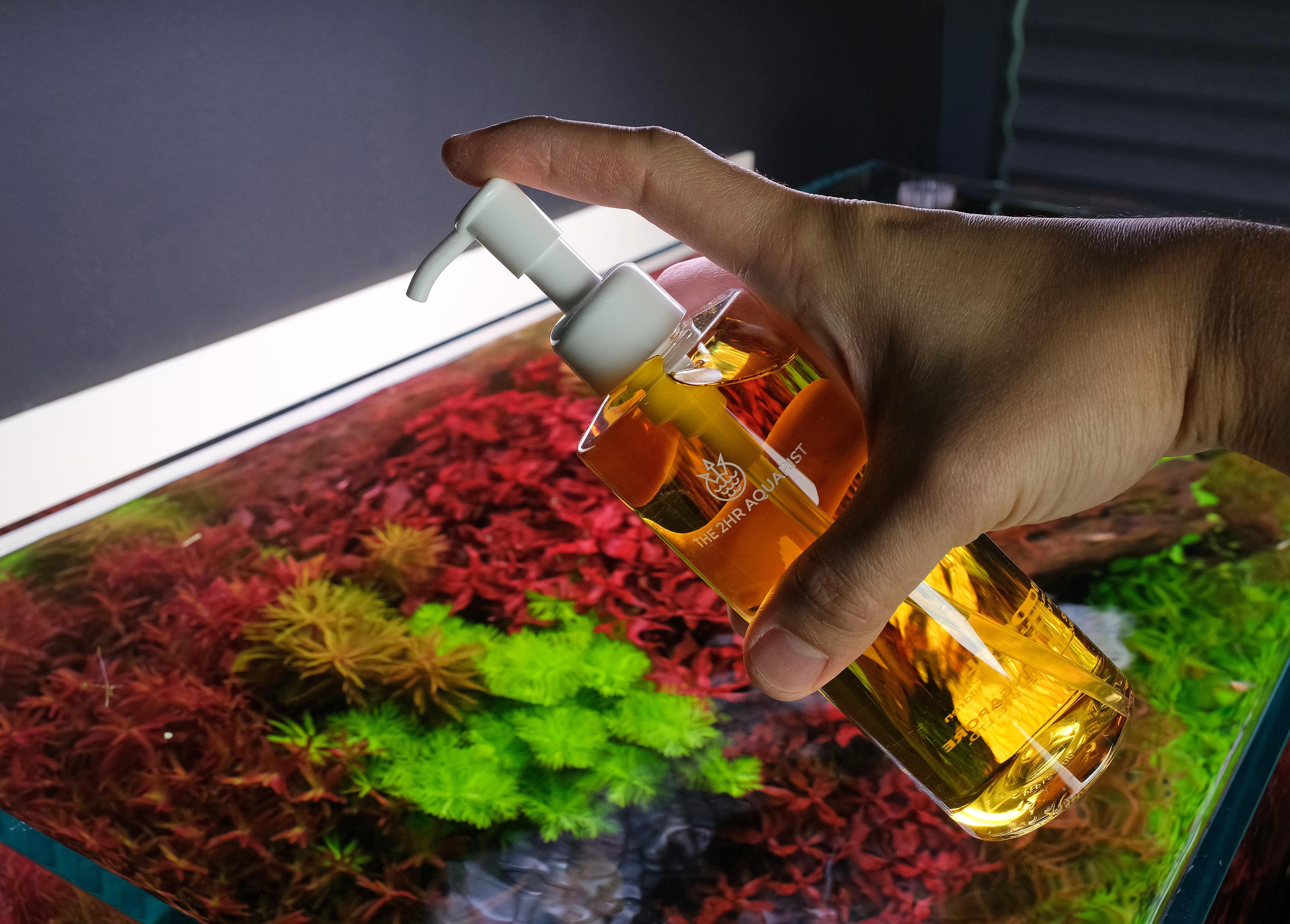 Hand holding a bottle of 2hr Aquarist APT3 above an aquarium