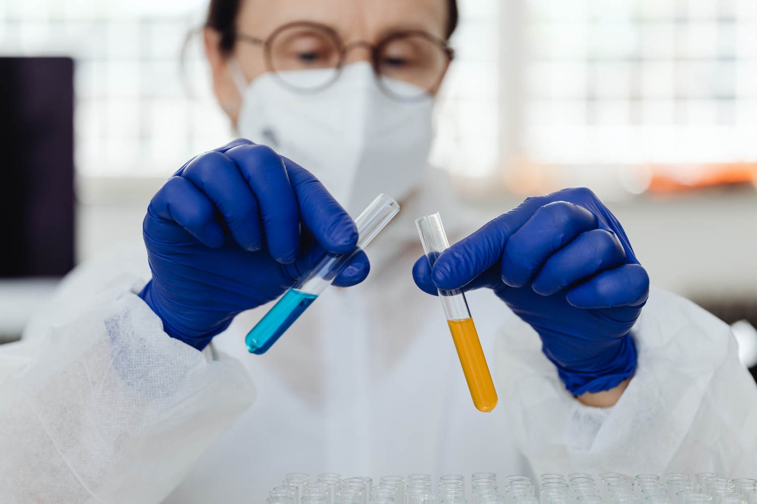 A technician in protective gear holds two test tubes, one filled with blue liquid and the other with yellow liquid, illustrating how private label gummies manufacturers test and monitor product quality during production.
