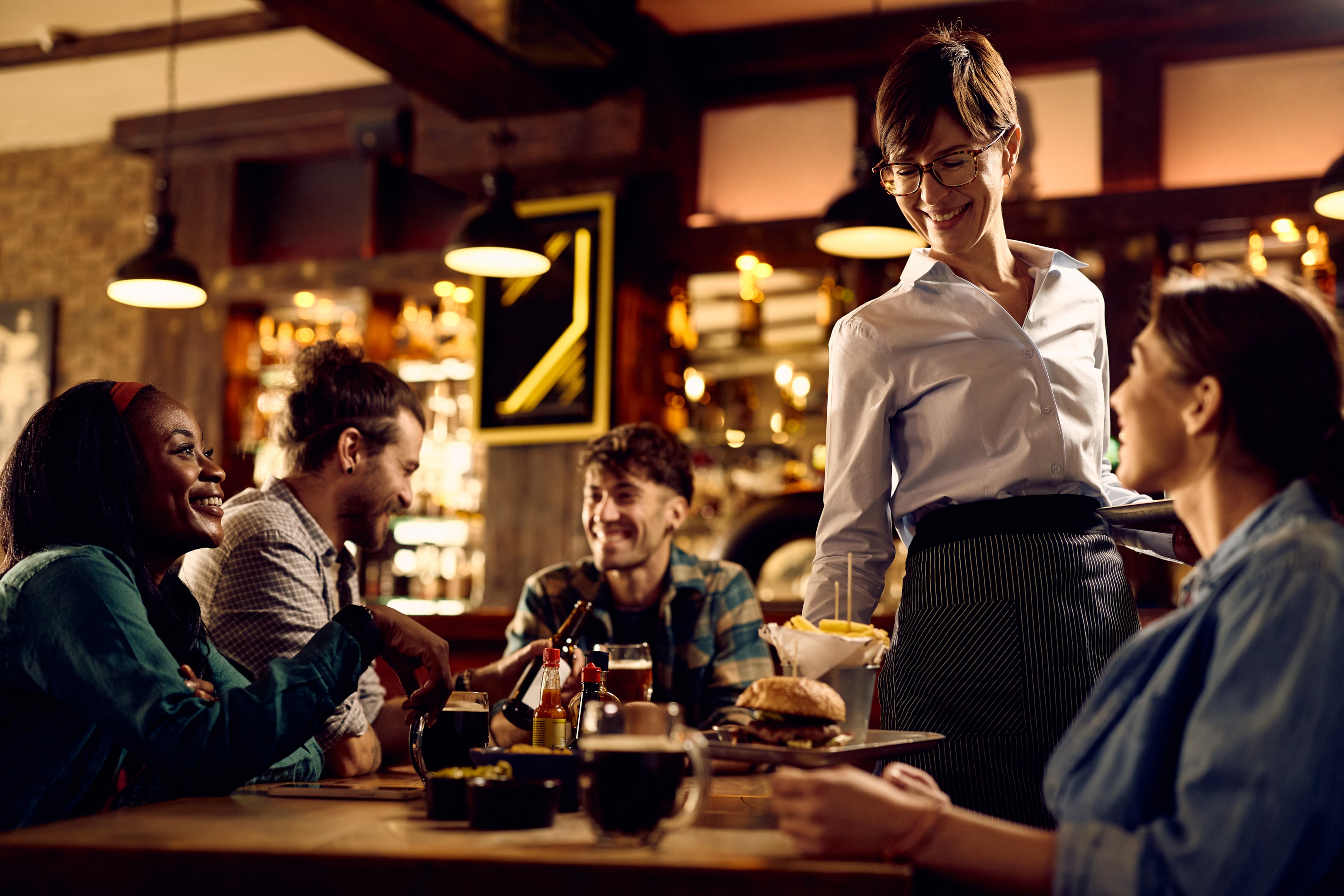 A restaurant server delivers food to a table of happy, hungry guests