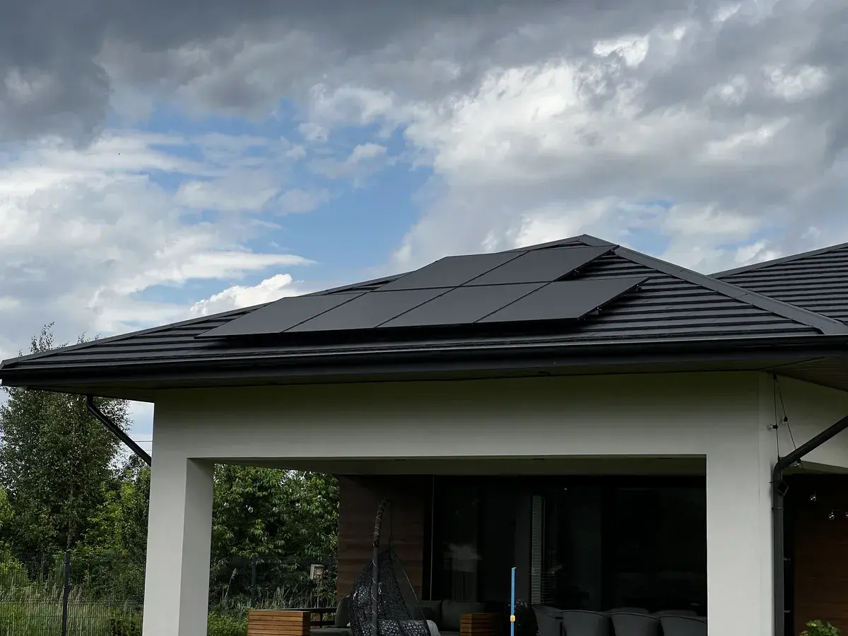 Nowoczesny dom jednorodzinny z panelami fotowoltaicznymi na dachu oraz pompą ciepła przy ścianie, co świadczy o realizacji przedsięwzięcia termomodernizacyjnego. Tego rodzaju inwestycje mogą pomóc właścicielom domów jednorodzinnych skorzystać z ulgi termomodernizacyjnej, poprawiając efektywność energetyczną budynku.