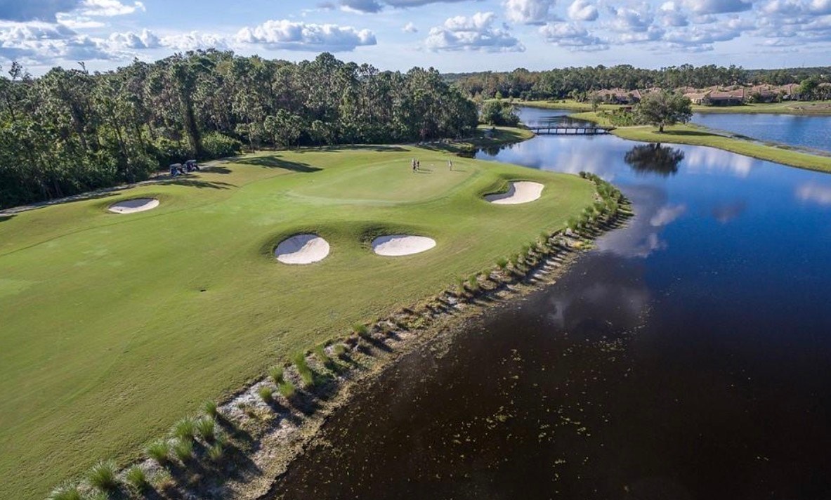 An aerial view of the Pelican Preserve community in Fort Myers, FL, showcases a stunning golf course intertwined with residential areas, all surrounded by lush preserves. This resort-style community features beautifully framed homes, a spacious pool deck, and serene cypress preserves, making it a perfect private tropical oasis for nature lovers.