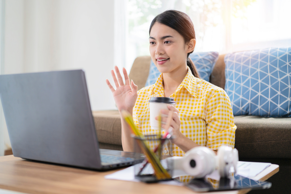 Young woman waving and smiling during a virtual coffee chat or remote interview