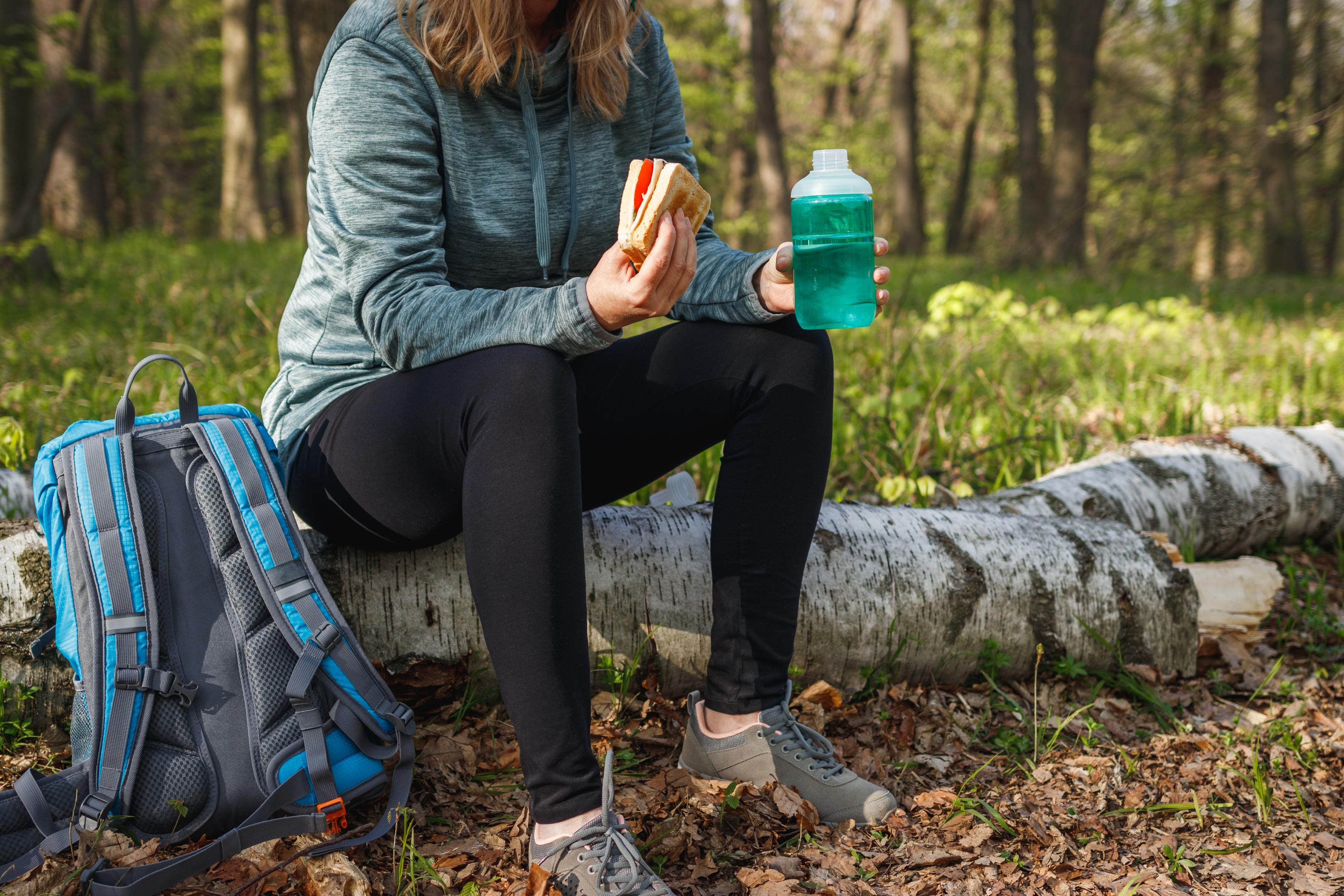 a woman holding a sandwish and bottled drink