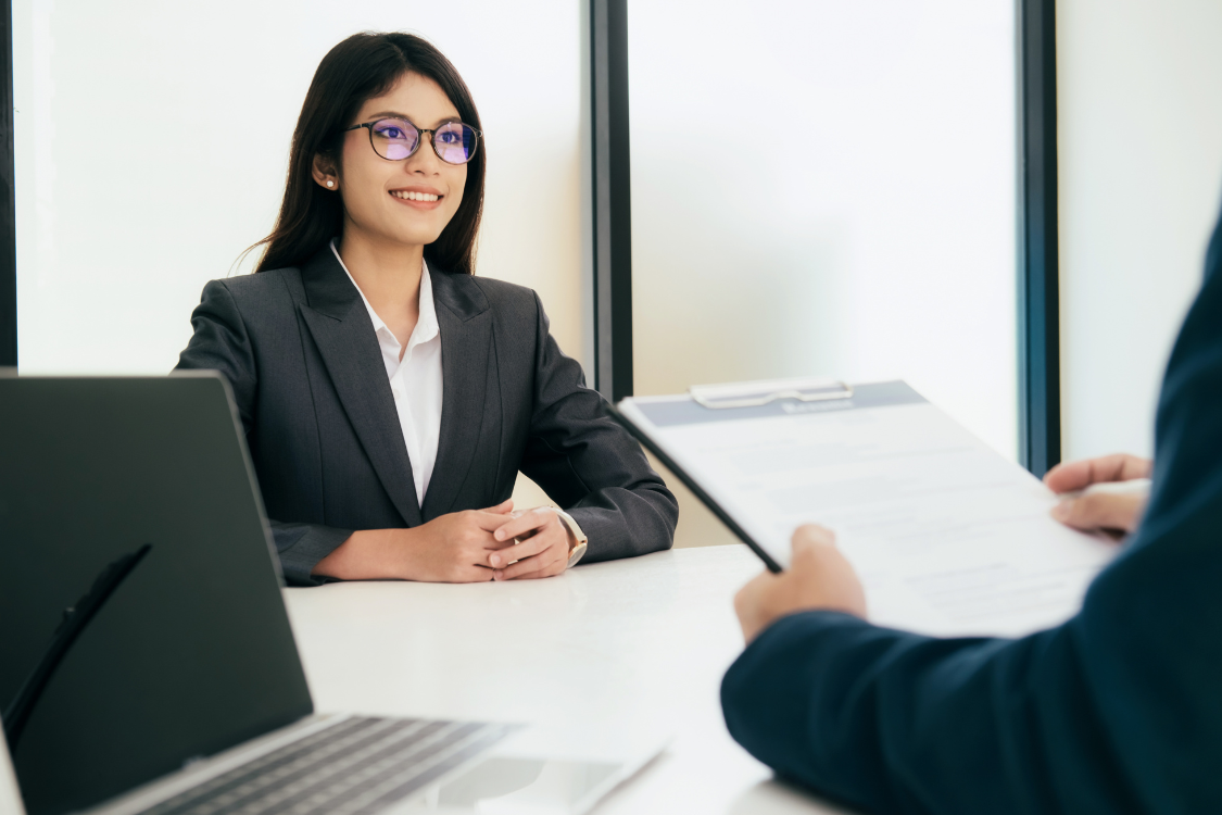 Confident woman in a blazer smiling during a broker consultation, illustrating the benefits of hiring professional help to sell a business.