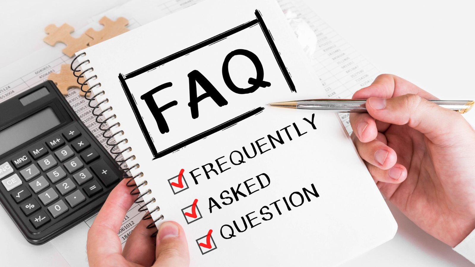 Hand holding a notebook labeled "FAQ" with checklist items for Frequently, Asked, and Question, next to a calculator.