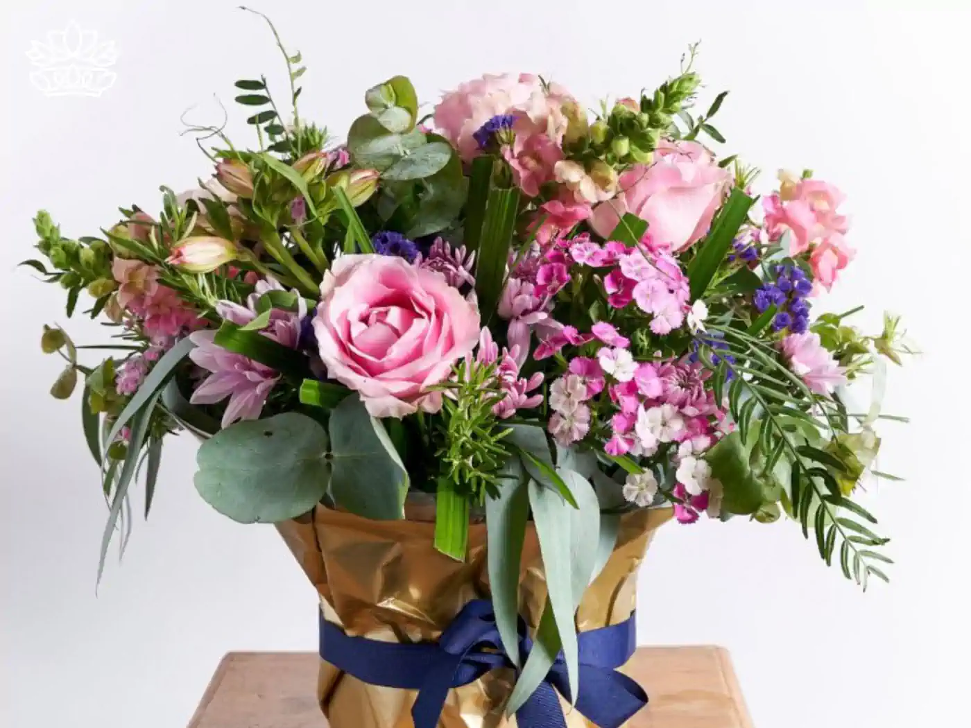 Elegant bouquet of soft pink roses, delicate purple asters, and lush greenery, wrapped in golden paper with a navy blue ribbon