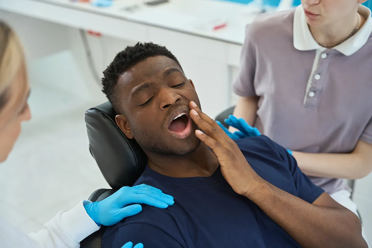 A patient expressing pain or discomfort while touching their face during a dental appointment
