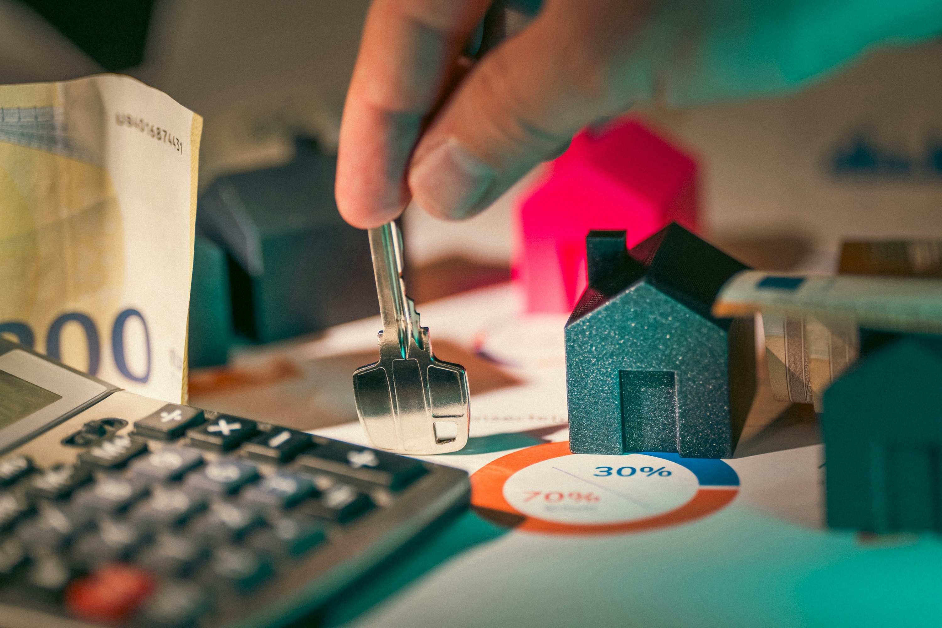 Real estate investor holds house key next to small model of house and calculator.