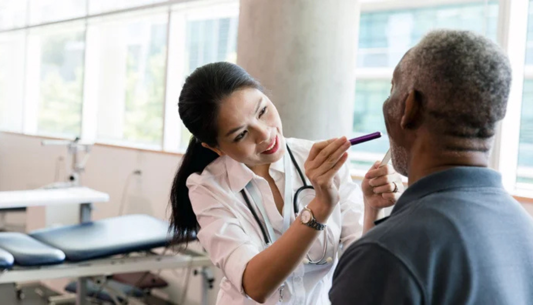 Lege lyser inn i munnen på eldre mann under halsundersøkelse.