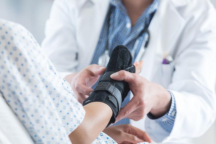 Doctor fitting wrist brace on injured patient in hospital gown during personal injury medical treatment