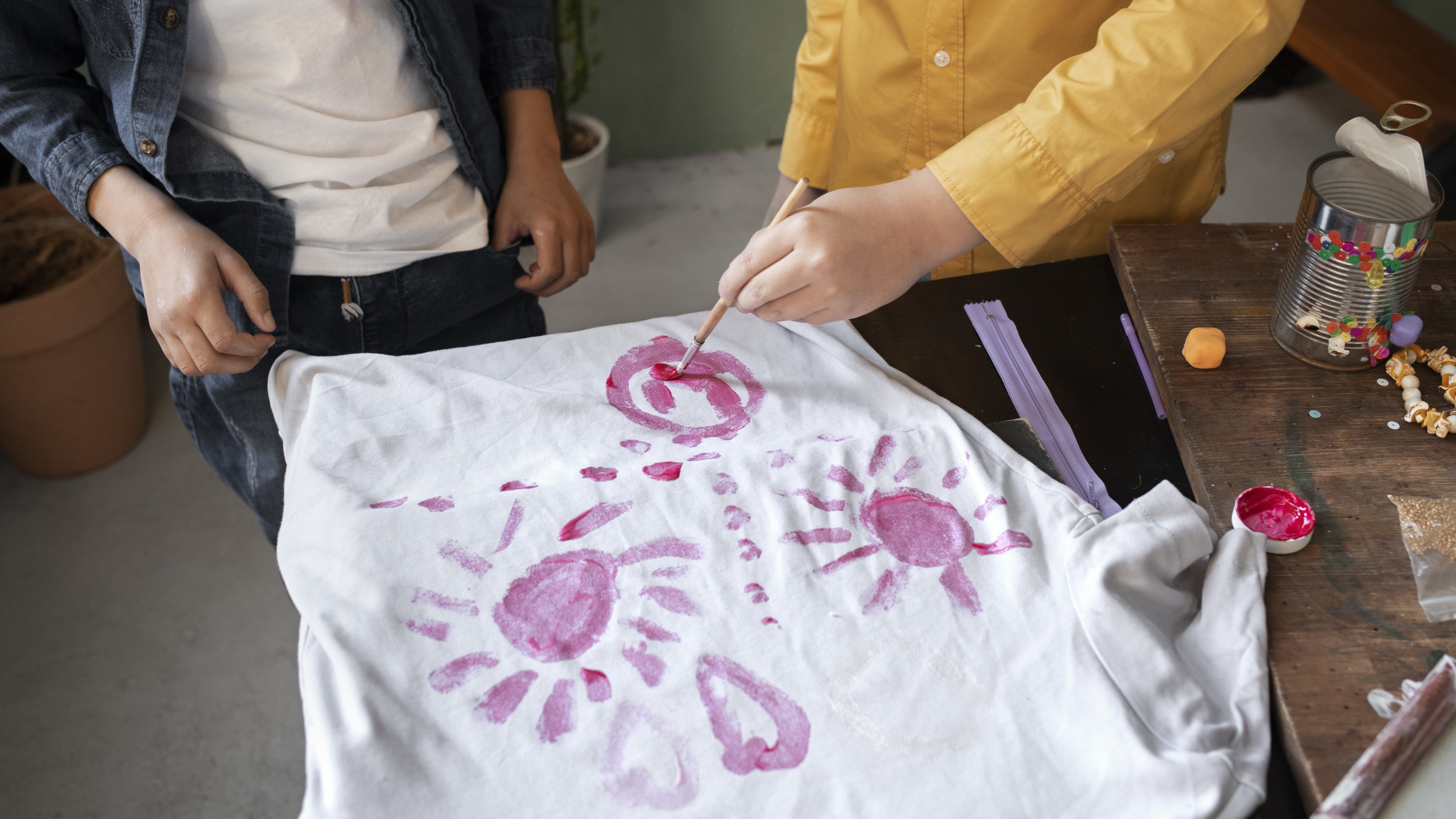 Na zdjęciu dzieci uczą się, jak malować na tkaninach koszulek poprzez pełne pociągnięcie pędzla.