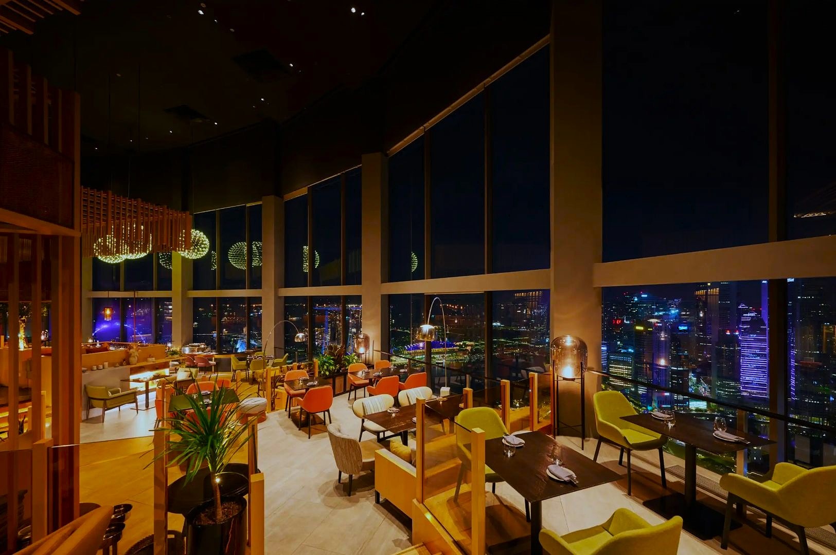Upscale restaurant interior with modern furniture and warm lighting, featuring large windows offering a stunning city skyline view at night. Cozy ambiance.