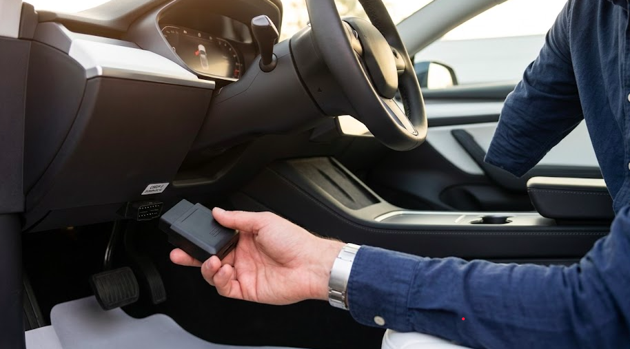 Person installing a GPS tracker into a car's OBD-II port under the dashboard
