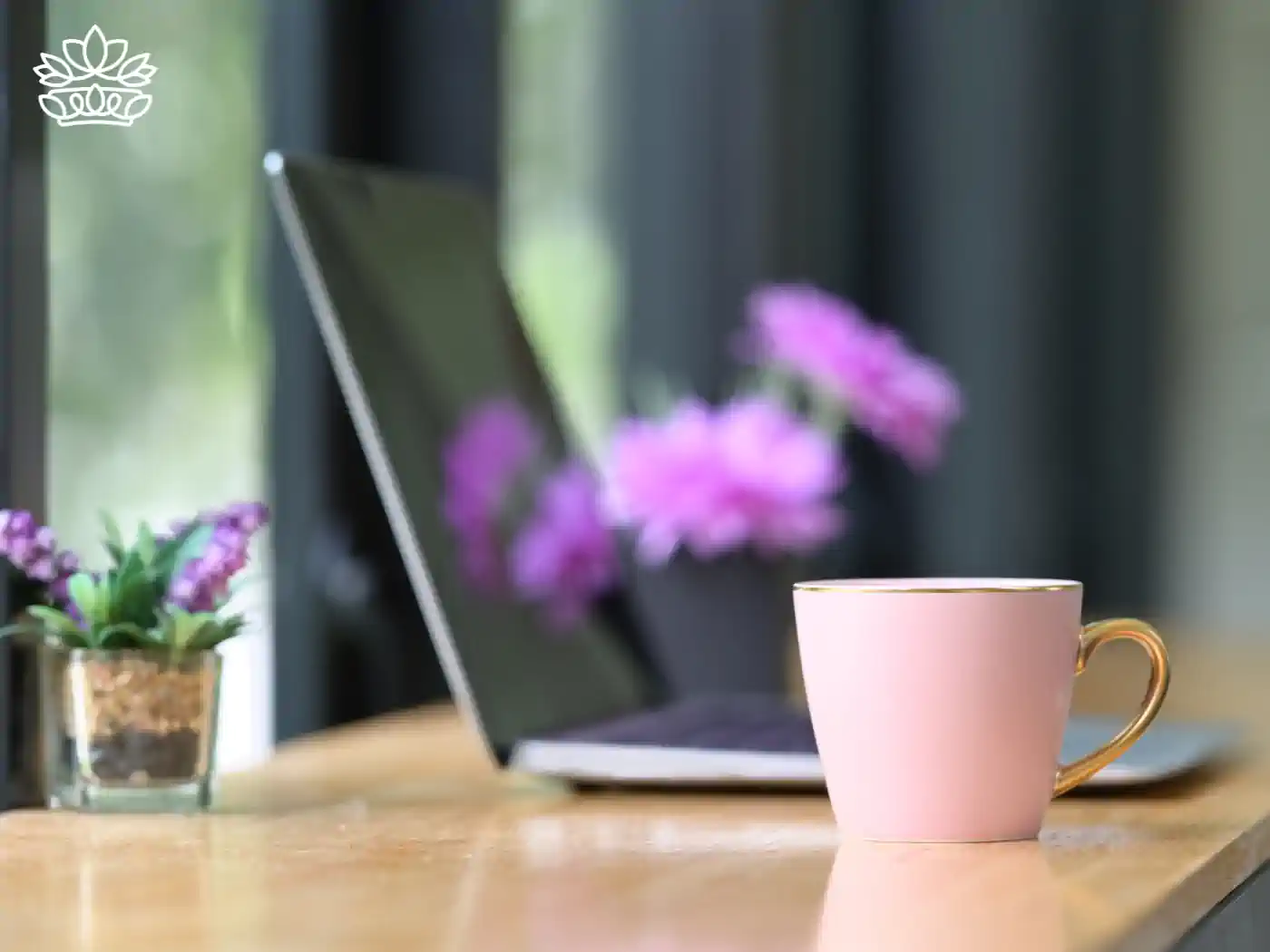 A stylish office setup featuring purple flowers and a pink mug beside a laptop. Fabulous Flowers and Gifts. Office Desk Flowers Collection.