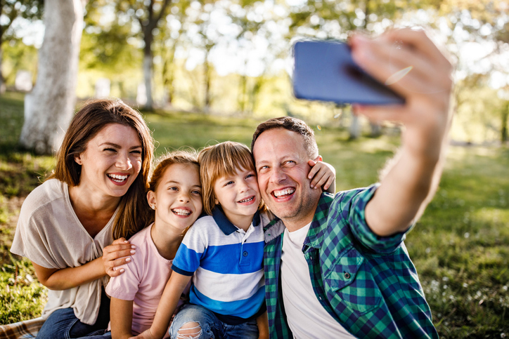 Happy young family of four smiling for a photo in a park. 