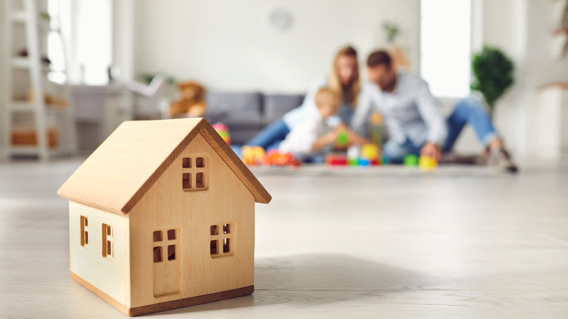 Lenders Mortgage Insurance (LMI) - Parents playing with their baby and there is a dummy wooden house in front of them