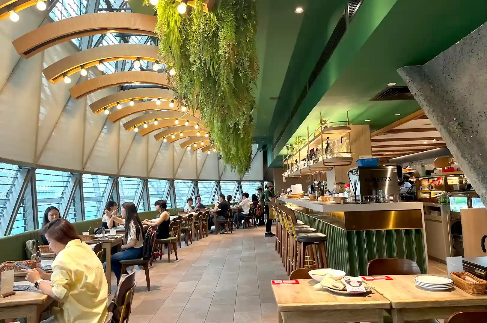 A vibrant cafe interior in Singapore featuring a stylish green bar counter, hanging plants, and patrons enjoying coffee and brunch.